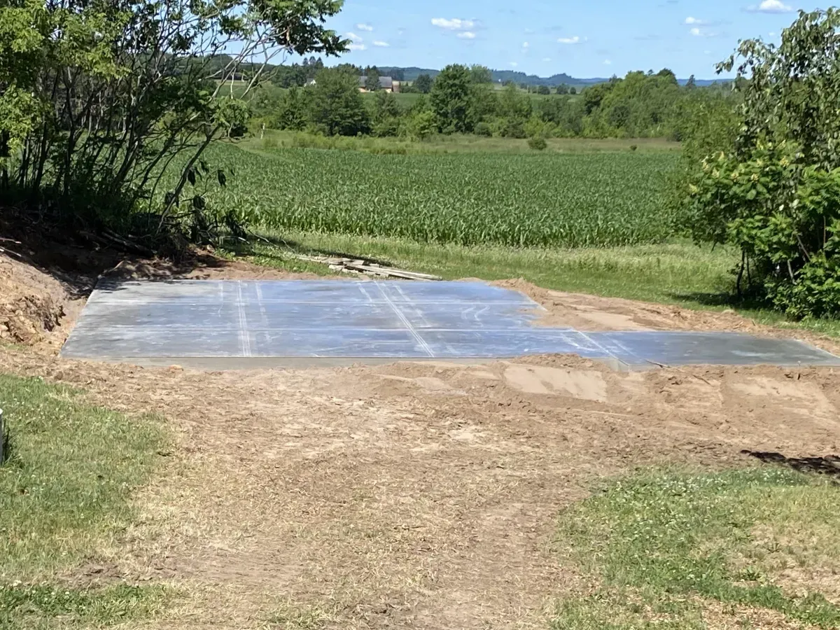Concrete slab in a grassy rural field with trees and open farmland in the background