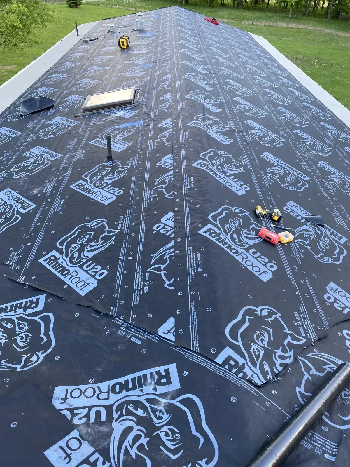 Roof covered with black synthetic underlayment, with tools and a board laid out along the ridge.