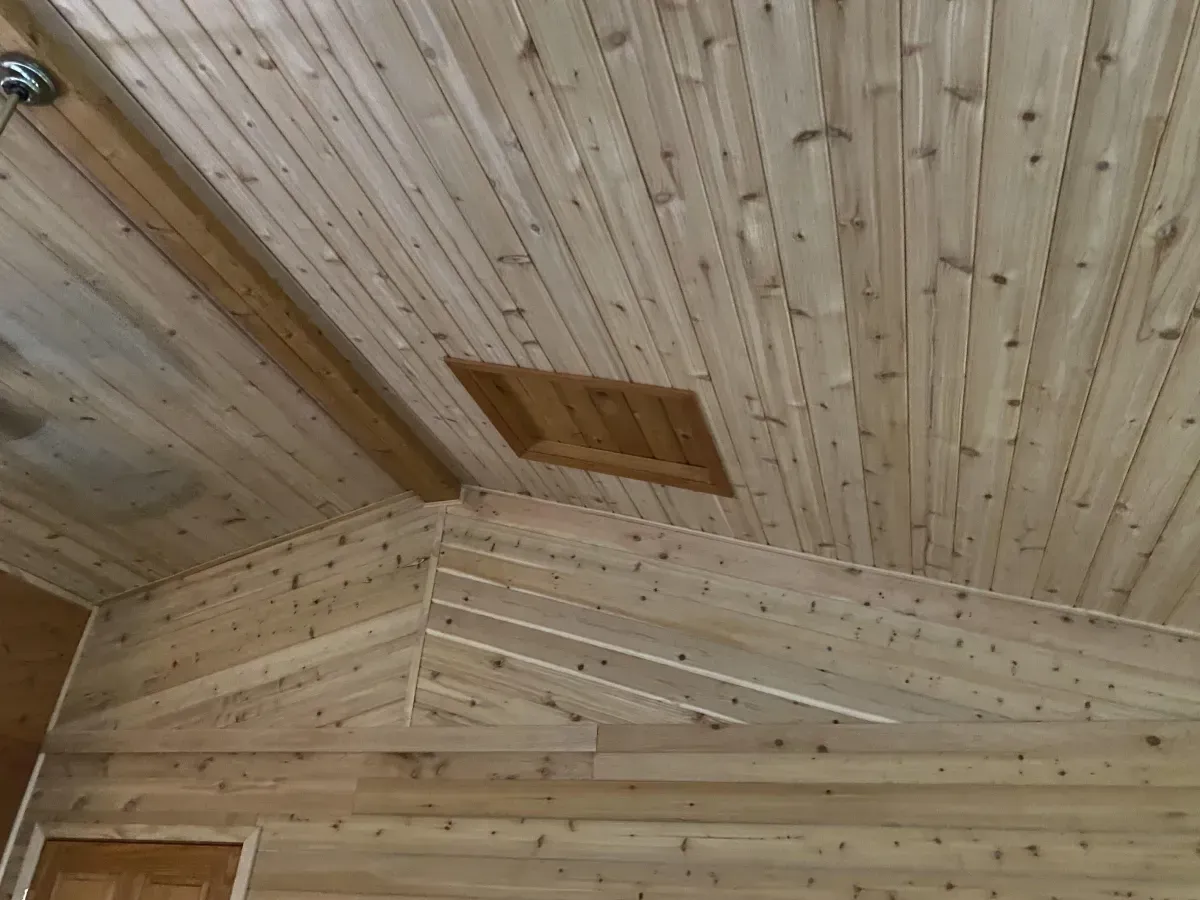 Wood-paneled ceiling and walls in a rustic interior, with a small attic vent panel.