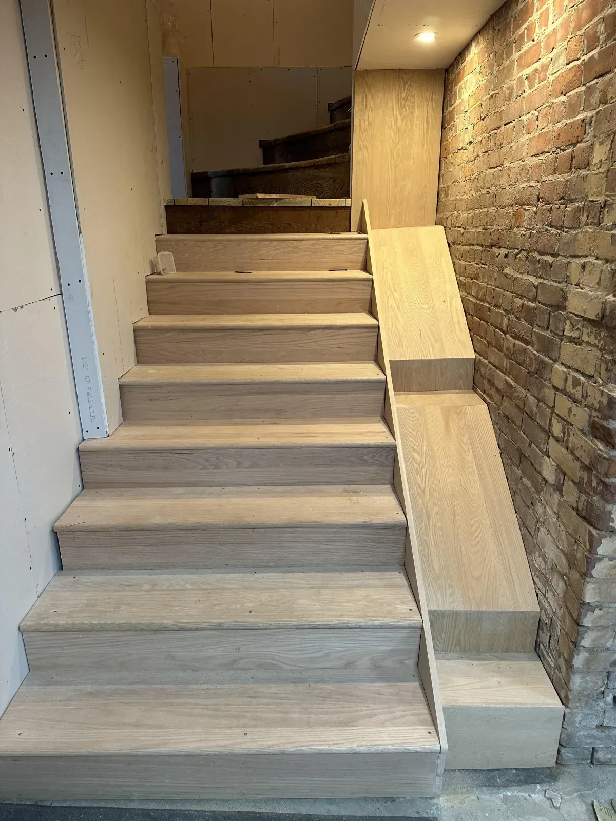 Narrow indoor staircase with unfinished wooden steps beside a brick wall in a hallway