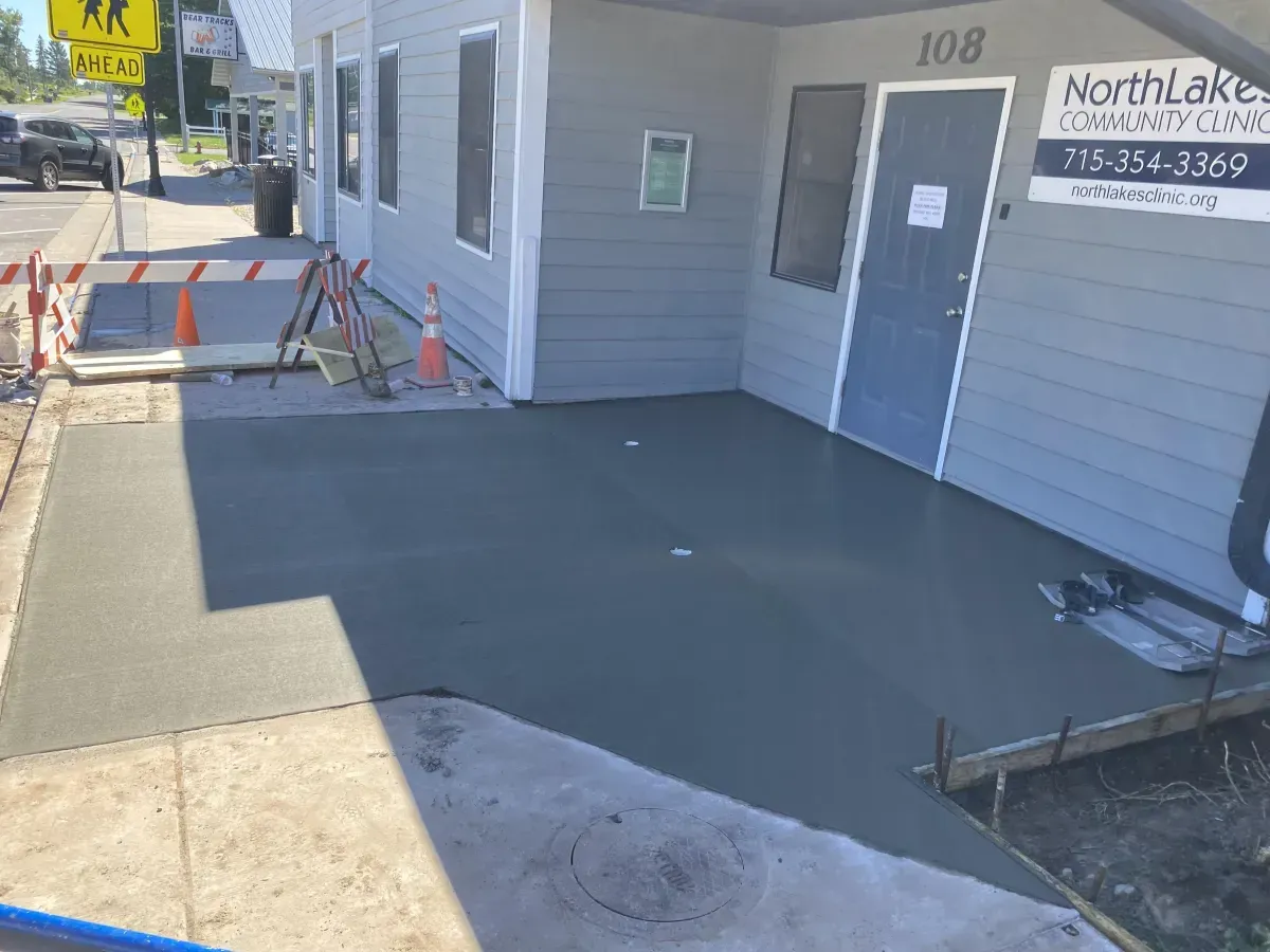 Accessible storefront entrance with fresh dark concrete ramp, orange cones, and barricade blocking the walkway