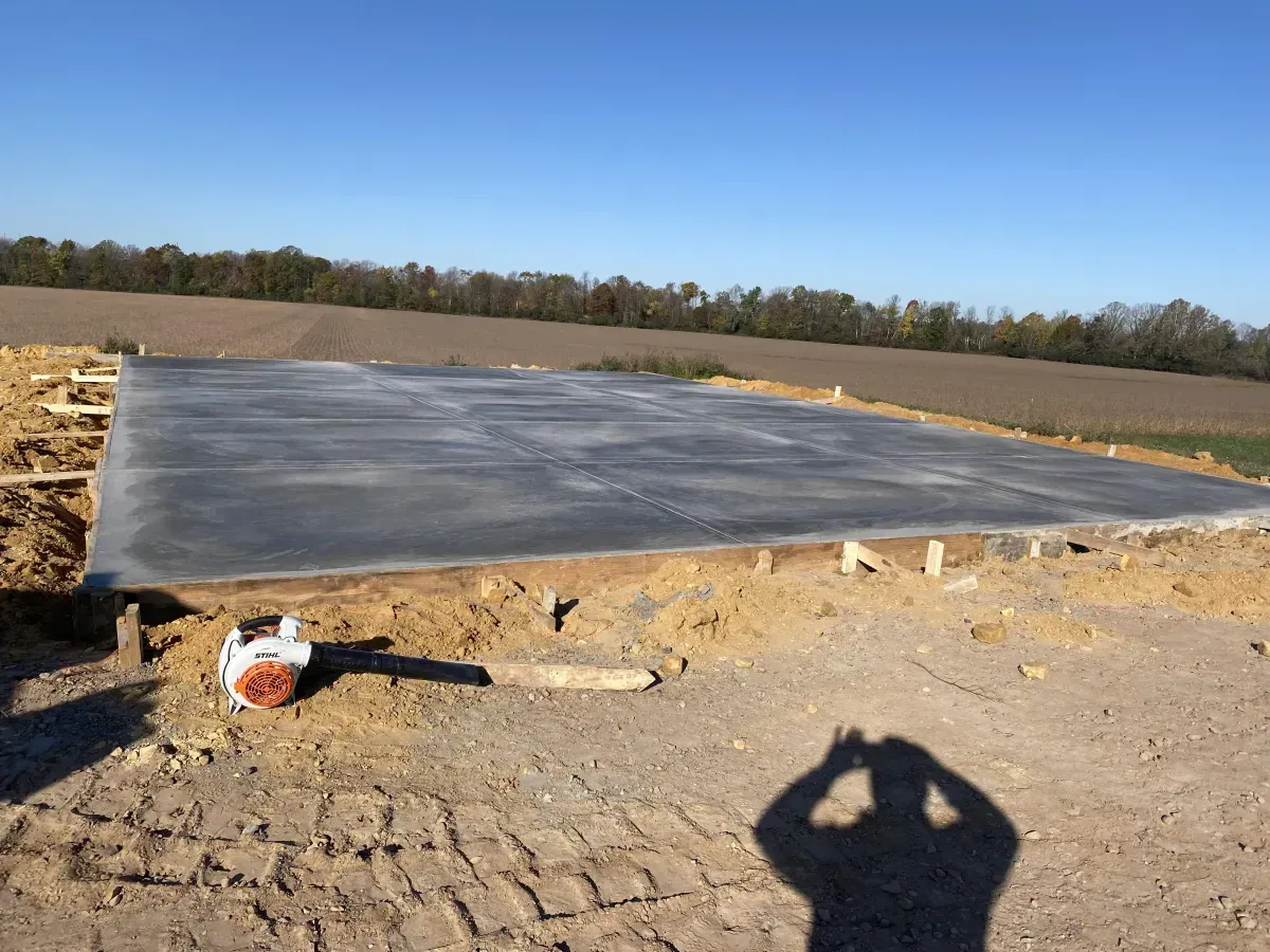 Large concrete slab under construction on a dirt lot, with trees in the distance and a clear blue sky.