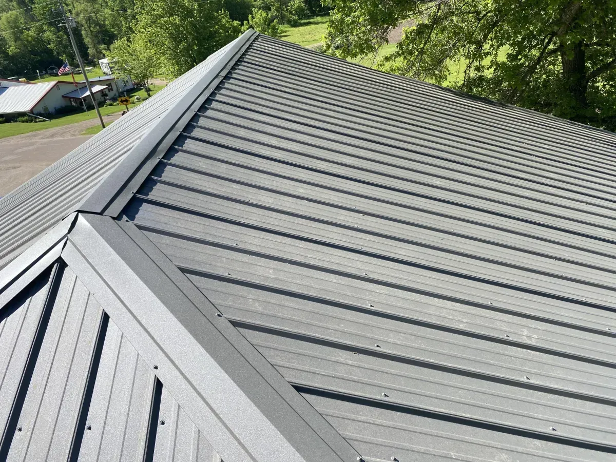 Gray metal roof with standing seams and a valley, viewed from above near trees