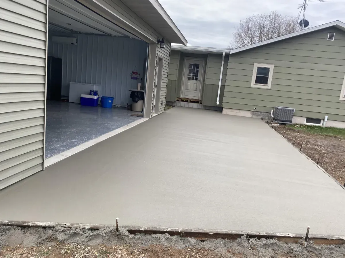 Fresh concrete driveway leading to an open garage and house entry under construction
