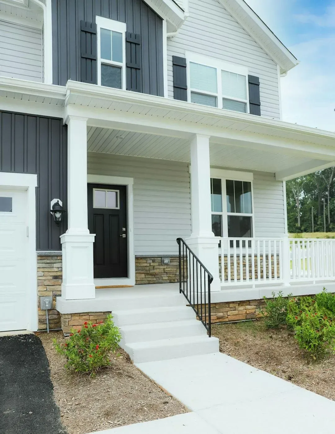 Two-story gray and white house with front porch, white railings, and a concrete walkway leading to the entrance