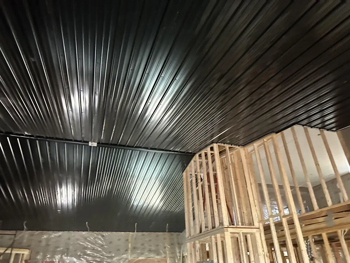 Dark corrugated metal ceiling above stacked wooden framing inside an unfinished building