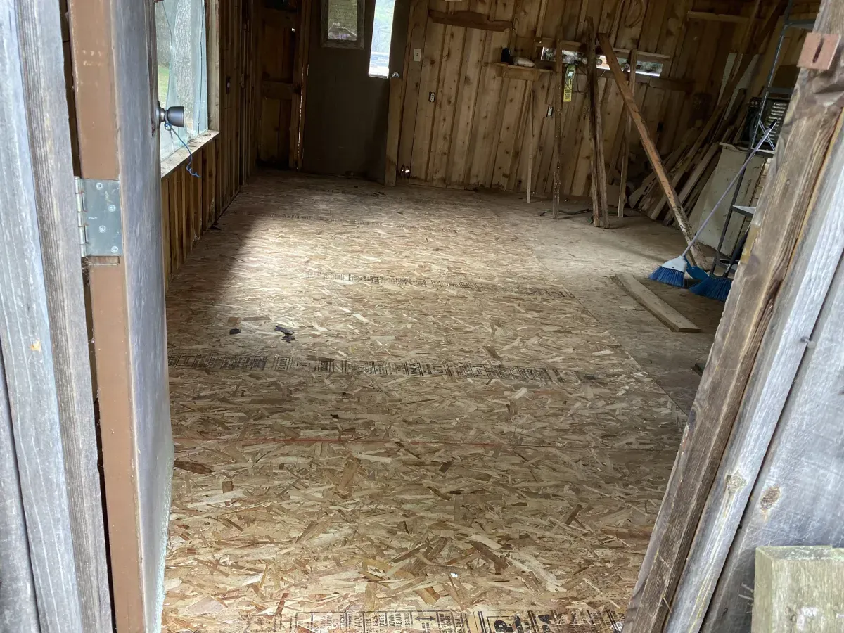 Empty unfinished wooden room with plywood floor and exposed wall studs, viewed from a doorway
