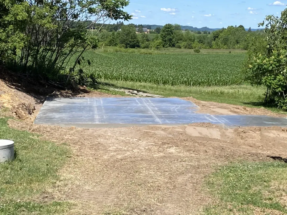 Gravel path leading to a tarp-covered area beside a green field and trees under a blue sky