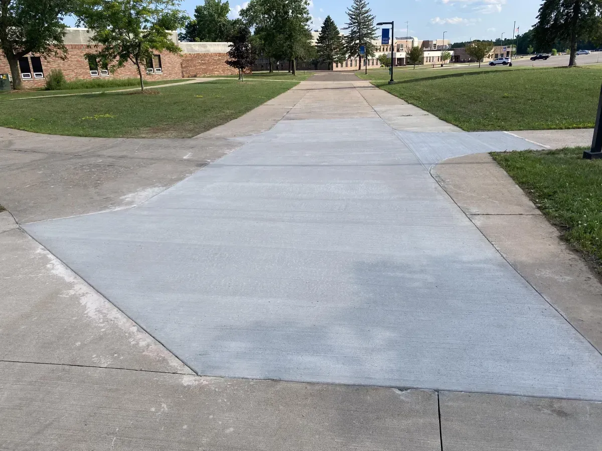 Concrete sidewalk leading through a grassy campus with buildings and trees in the distance