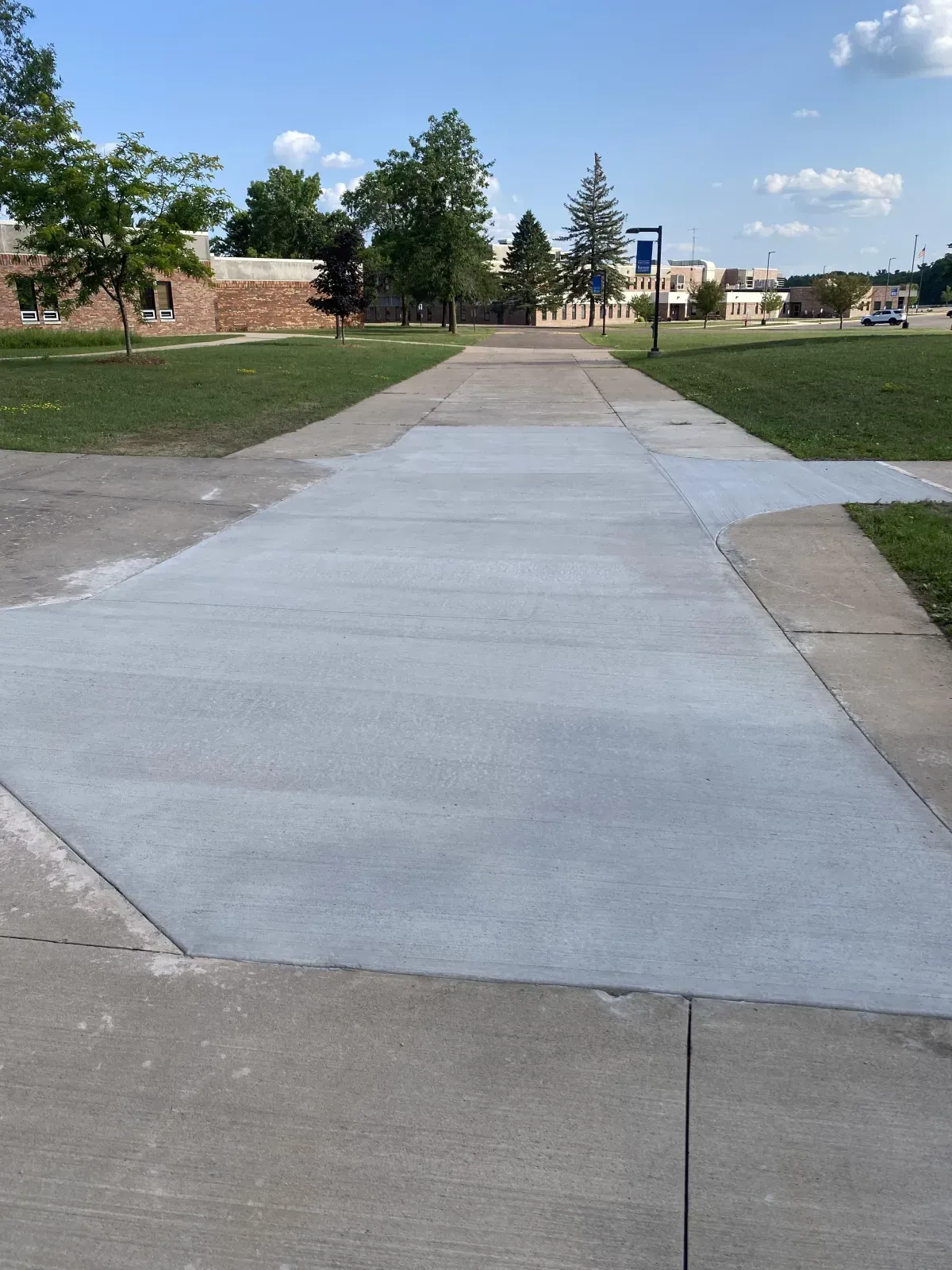 Concrete sidewalk through a grassy park with trees and a distant playground under a clear sky
