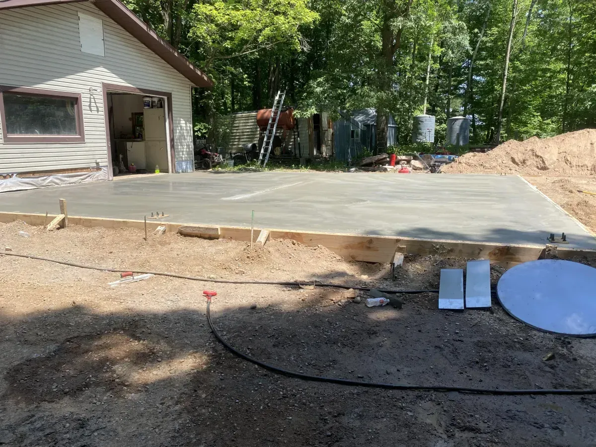 Driveway under construction beside a house, with fresh concrete, dirt piles, and work materials.