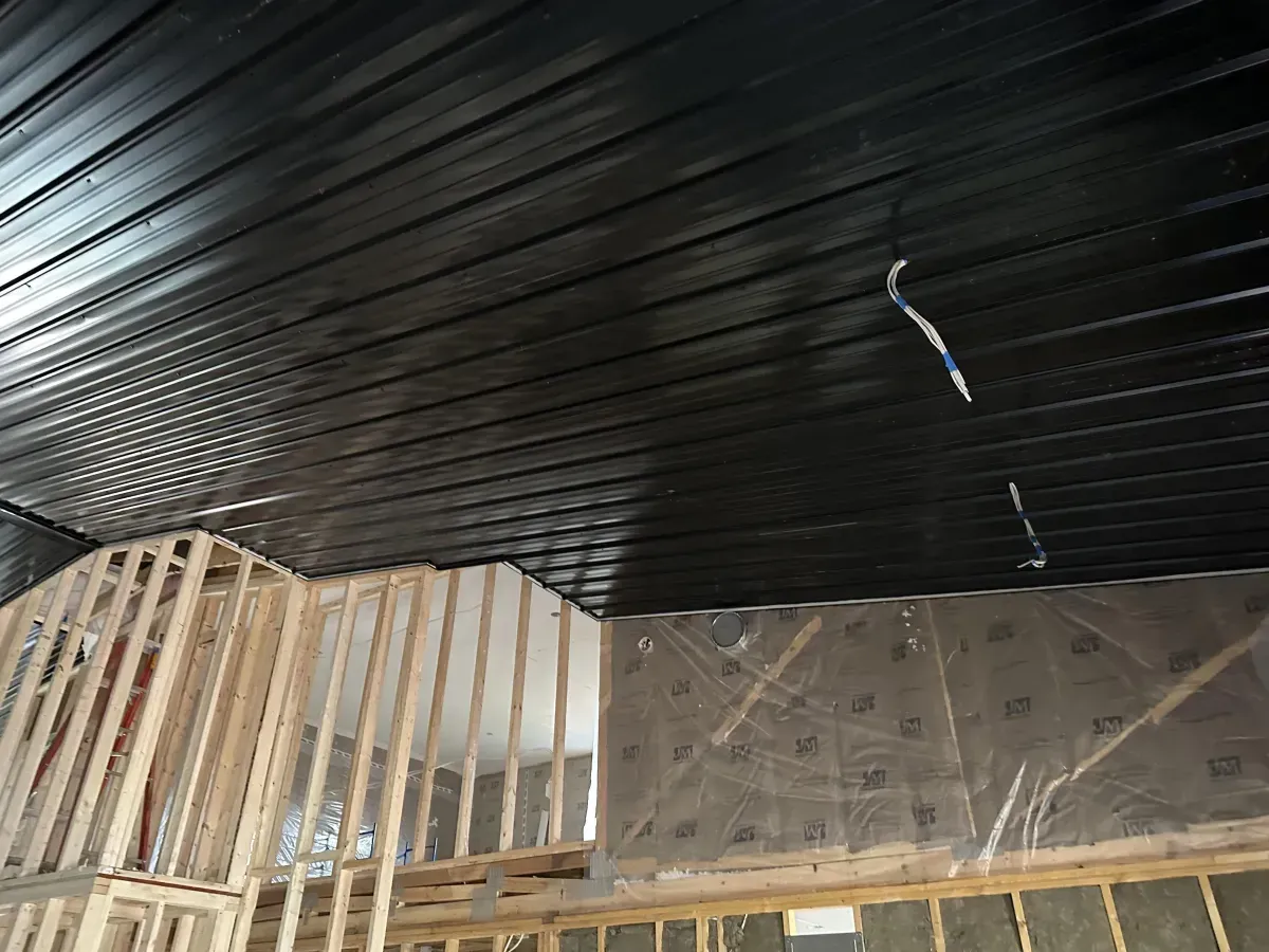 Partially finished interior with black ceiling, exposed wooden framing, and a brick wall under construction