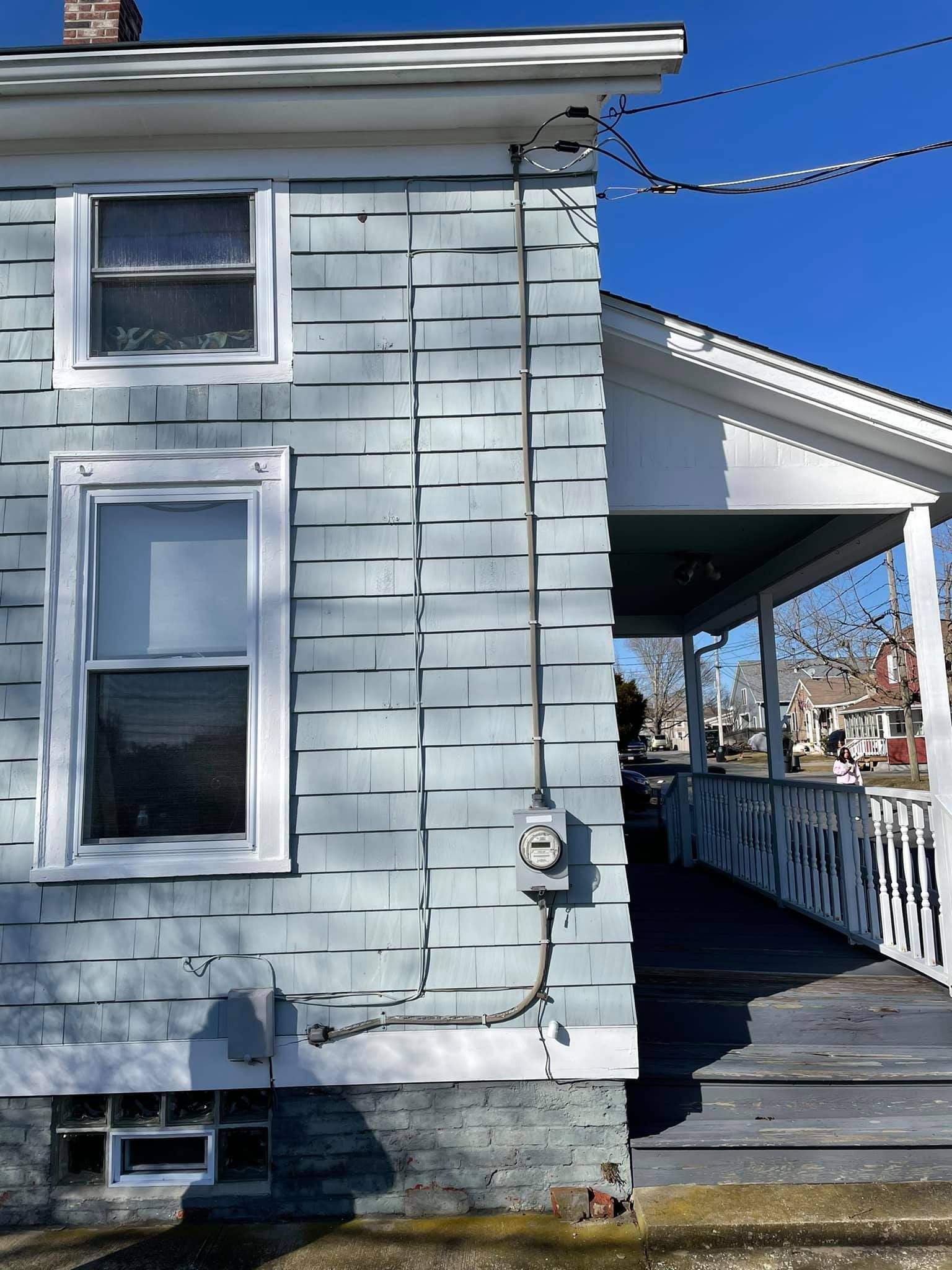 Side of a blue-gray shingle house with electrical wiring, windows, and a porch.