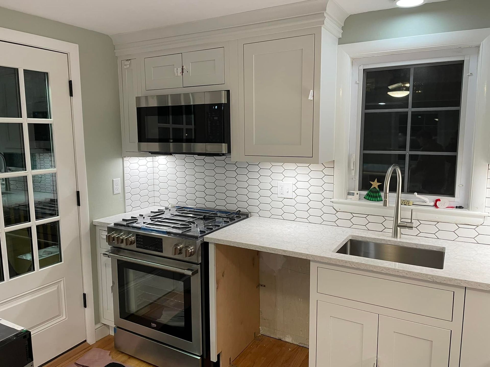 Kitchen with white cabinets, appliances, and backsplash, and a window over a sink.