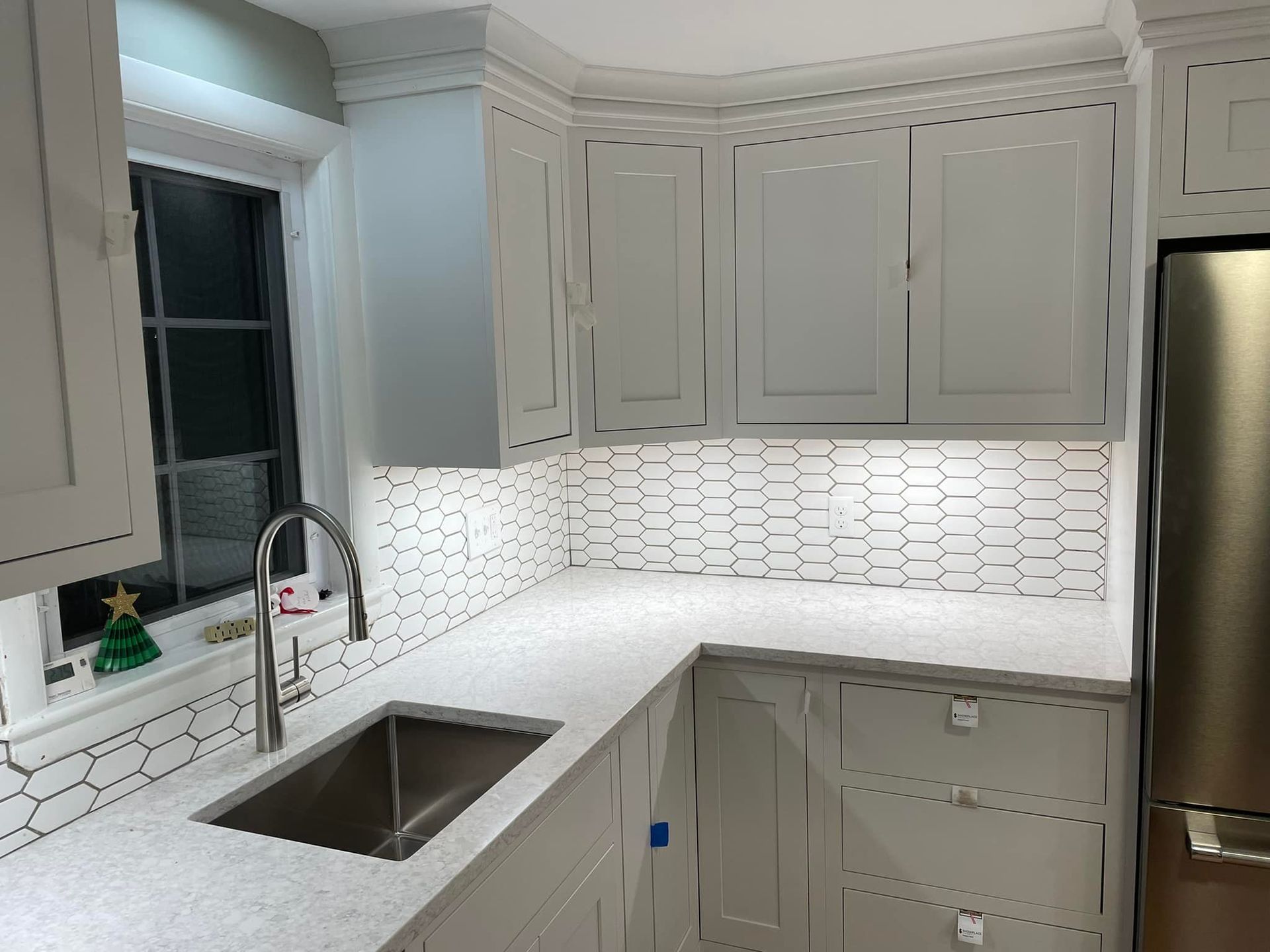 Kitchen with white cabinets, countertops, and backsplash; stainless steel sink and refrigerator.