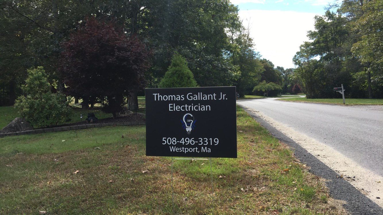 Sign for Thomas Gallant Jr., Electrician; black sign with name, profession, and phone number, roadside.