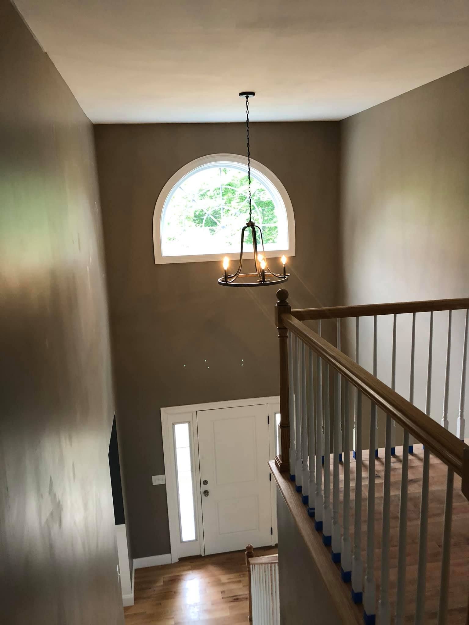 Entryway with a chandelier, arched window, white door, and staircase. Brown walls, light wood floors.