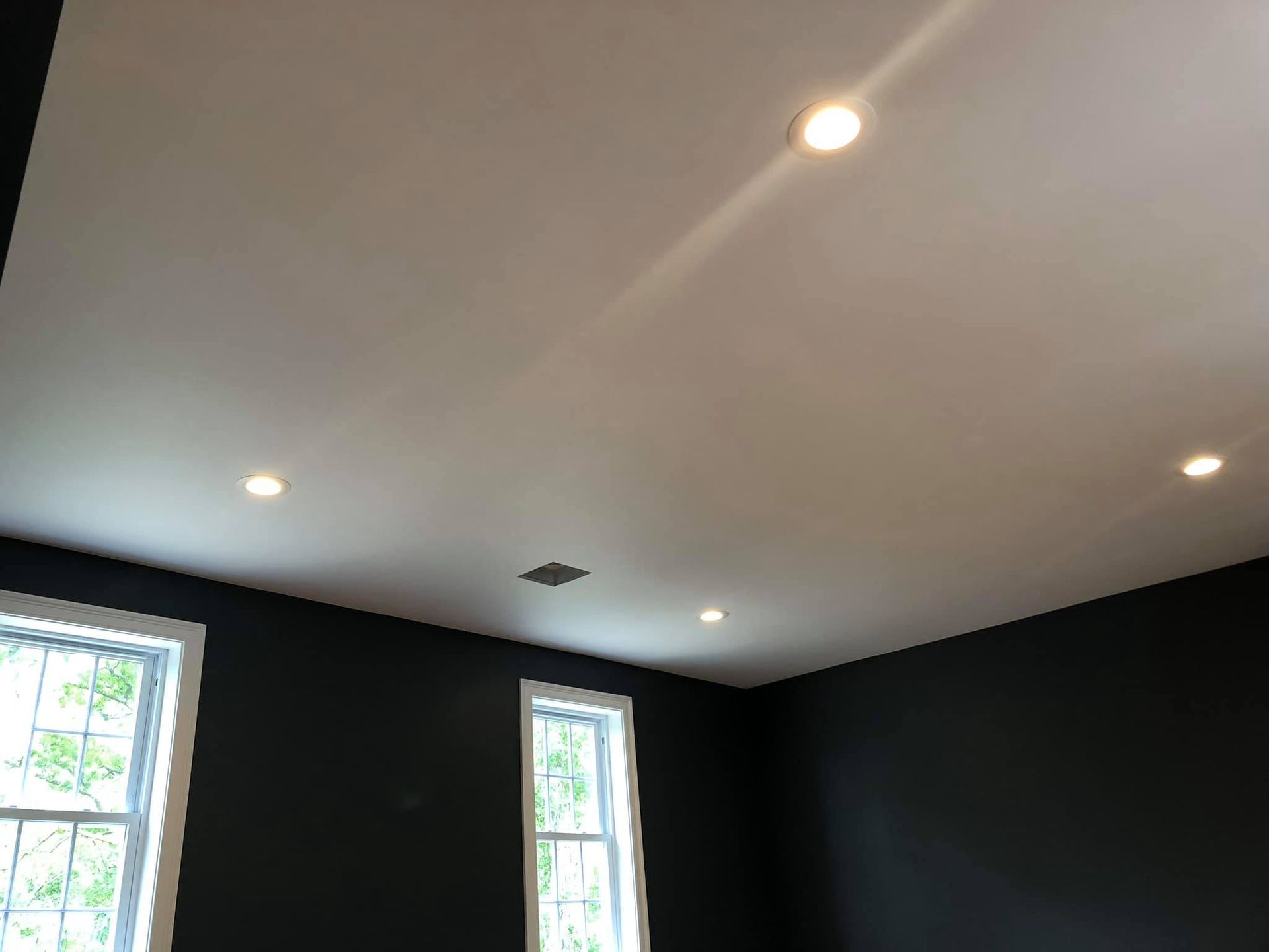 Ceiling with recessed lights in a room with dark walls and windows.