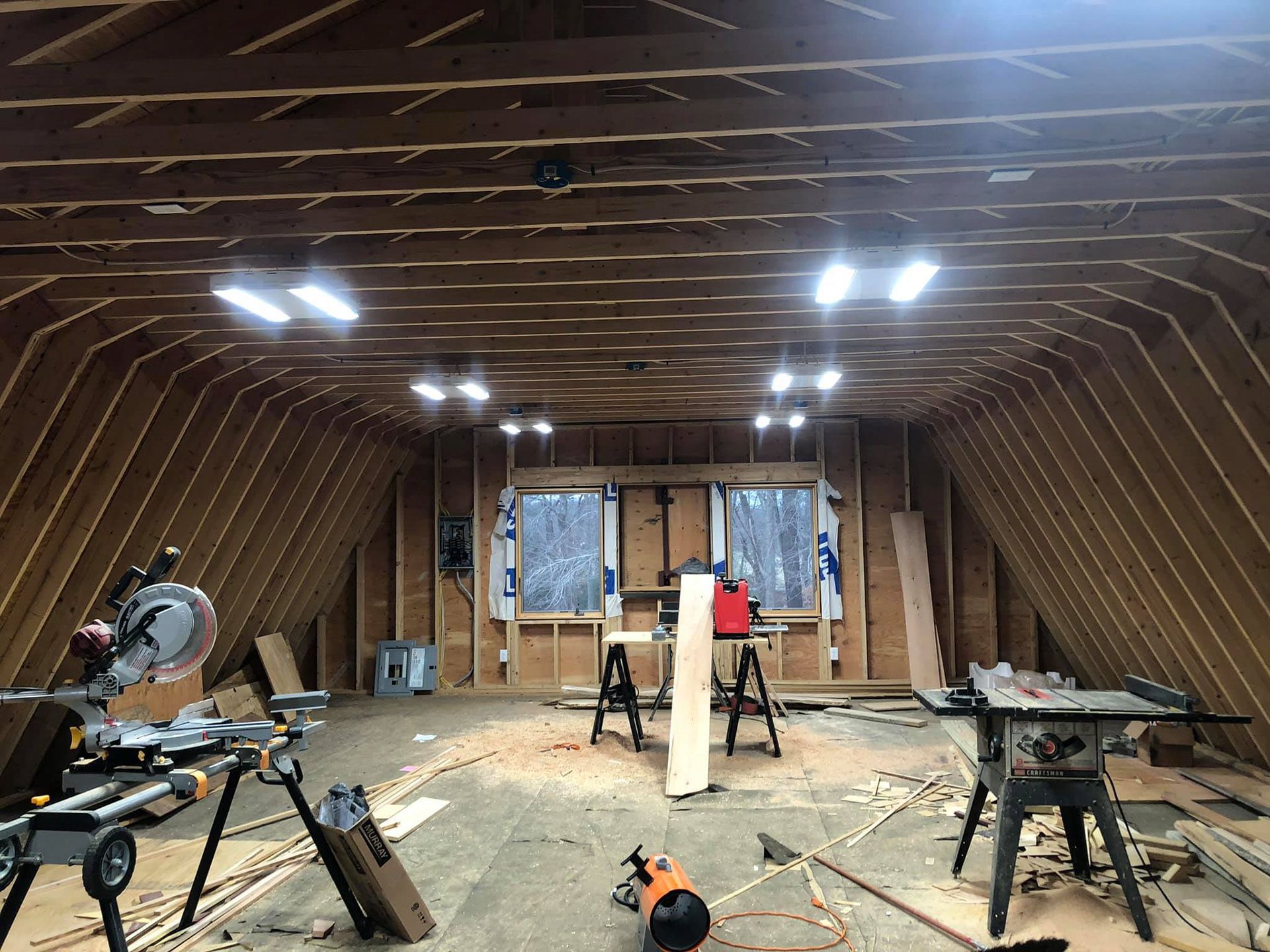 Attic workshop with exposed rafters, tools, and lights.