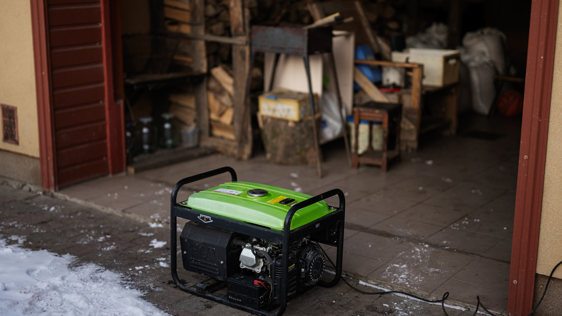 Green and black generator outside a shed, snow on the ground.