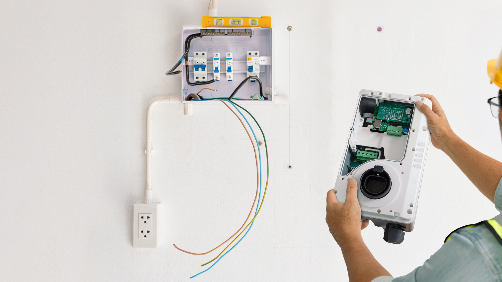 Electrician working on electrical box and charging station on a white wall.