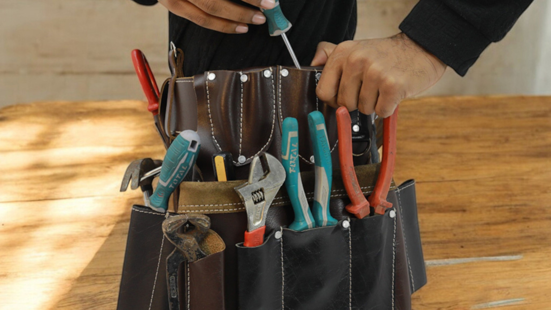 Person with a tool belt selects a screwdriver. Other tools, including pliers and a wrench, are visible.