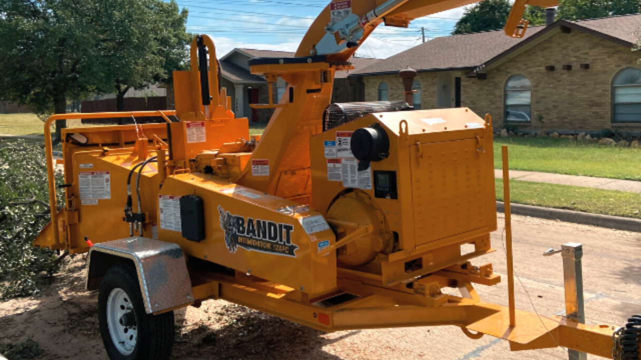A bright yellow Bandit wood chipper parked on a residential driveway on a sunny day.
