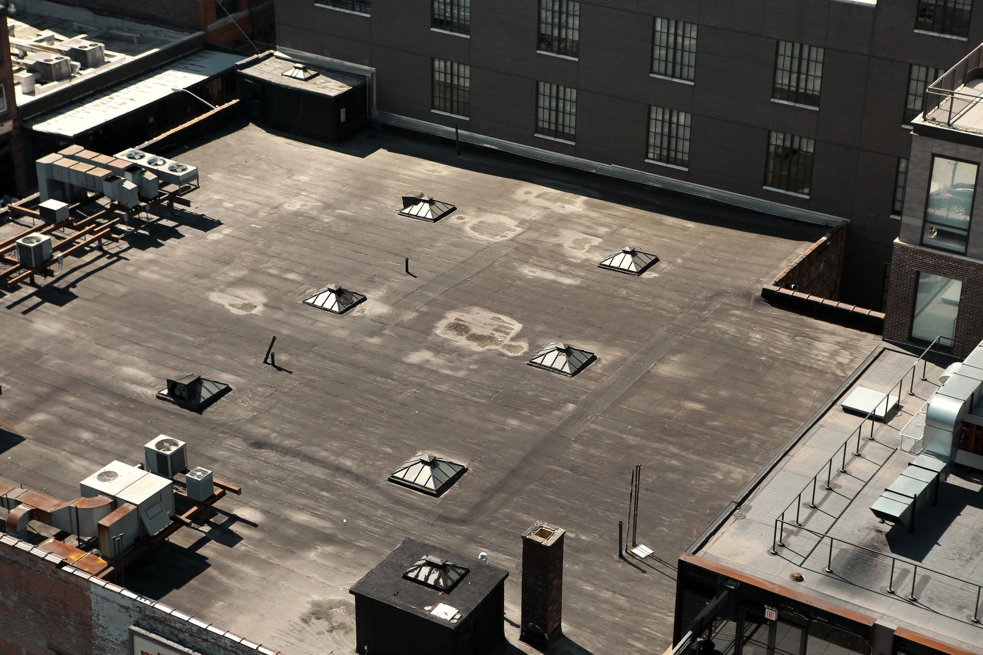 Person rolling out black roofing material on an OSB plywood roof, using a heat gun.