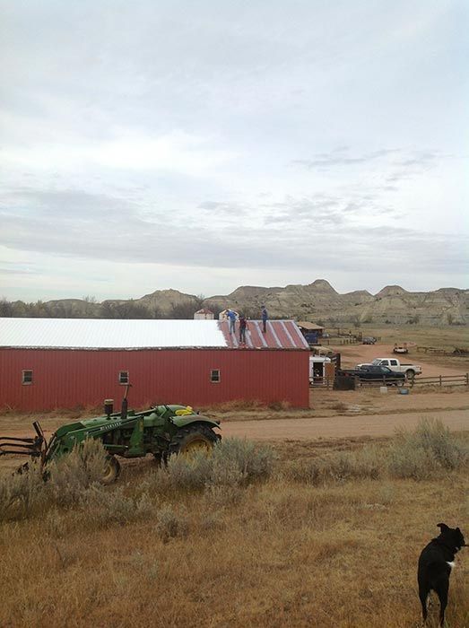 Person on rooftop using a drill to repair the roofing. The roof is gray with leaves.
