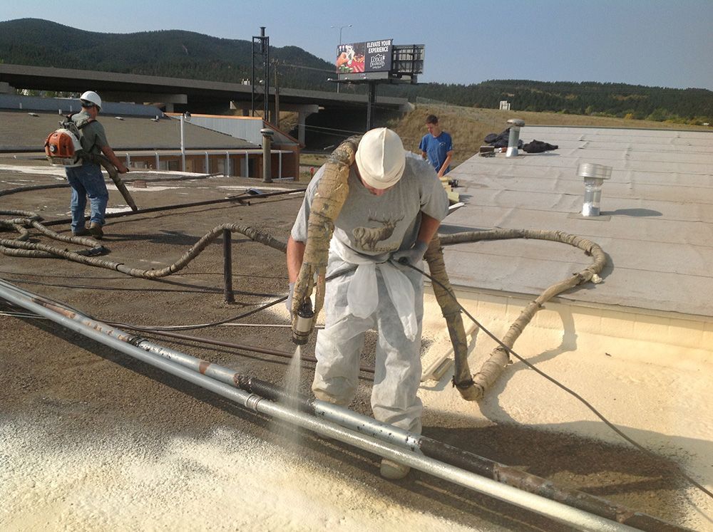 Two construction workers install metal roofing on a steel frame, wearing safety vests against a blue sky.