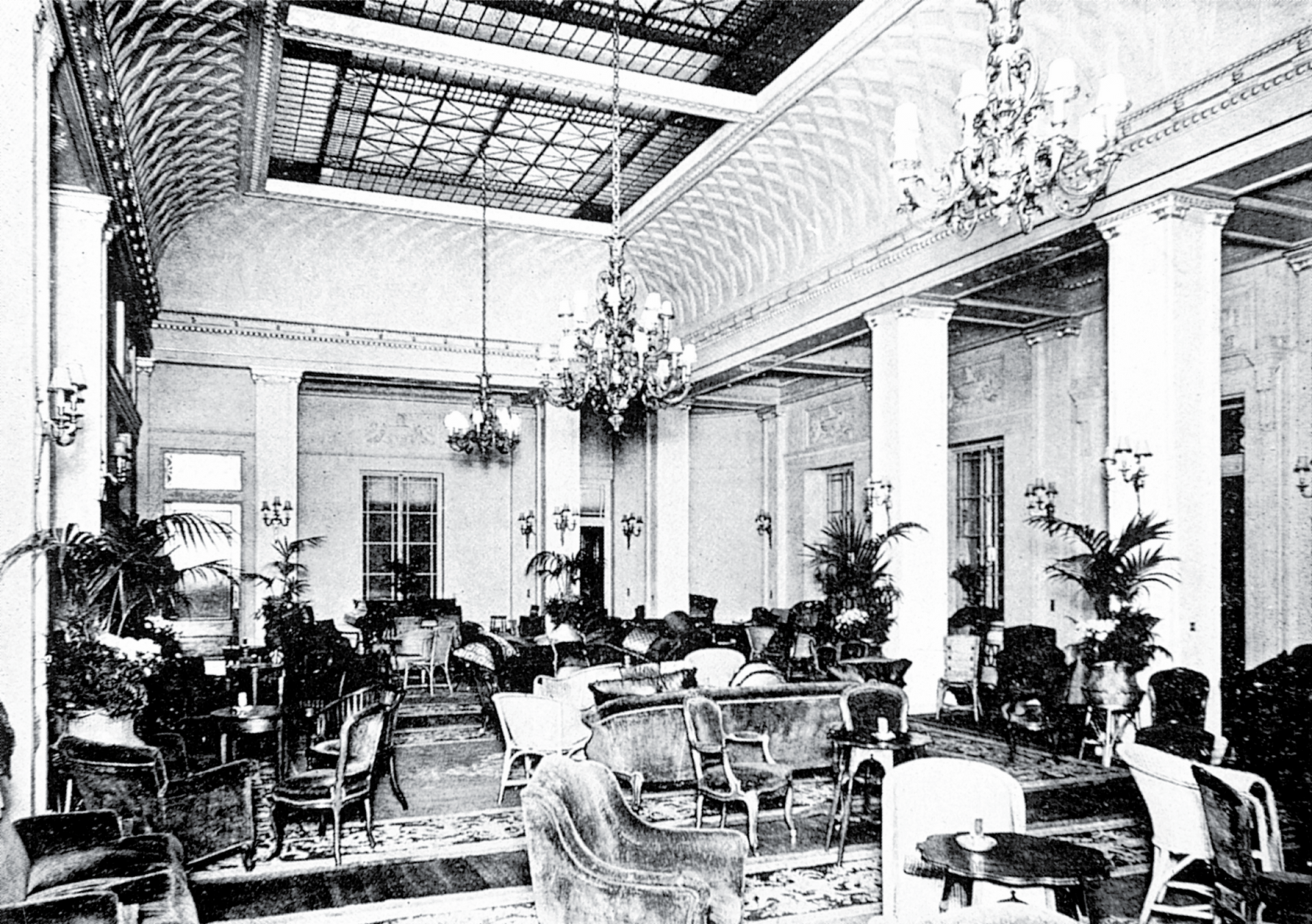 Interior of a grand room with ornate columns, chandeliers, and seating areas.