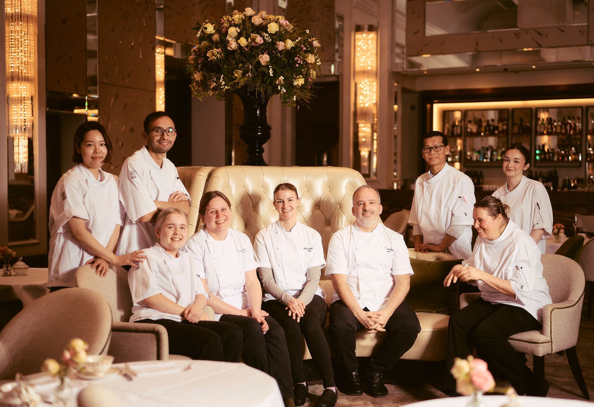 Restaurant staff posing for a photo. They are in white uniforms and are near a booth and a floral arrangement.