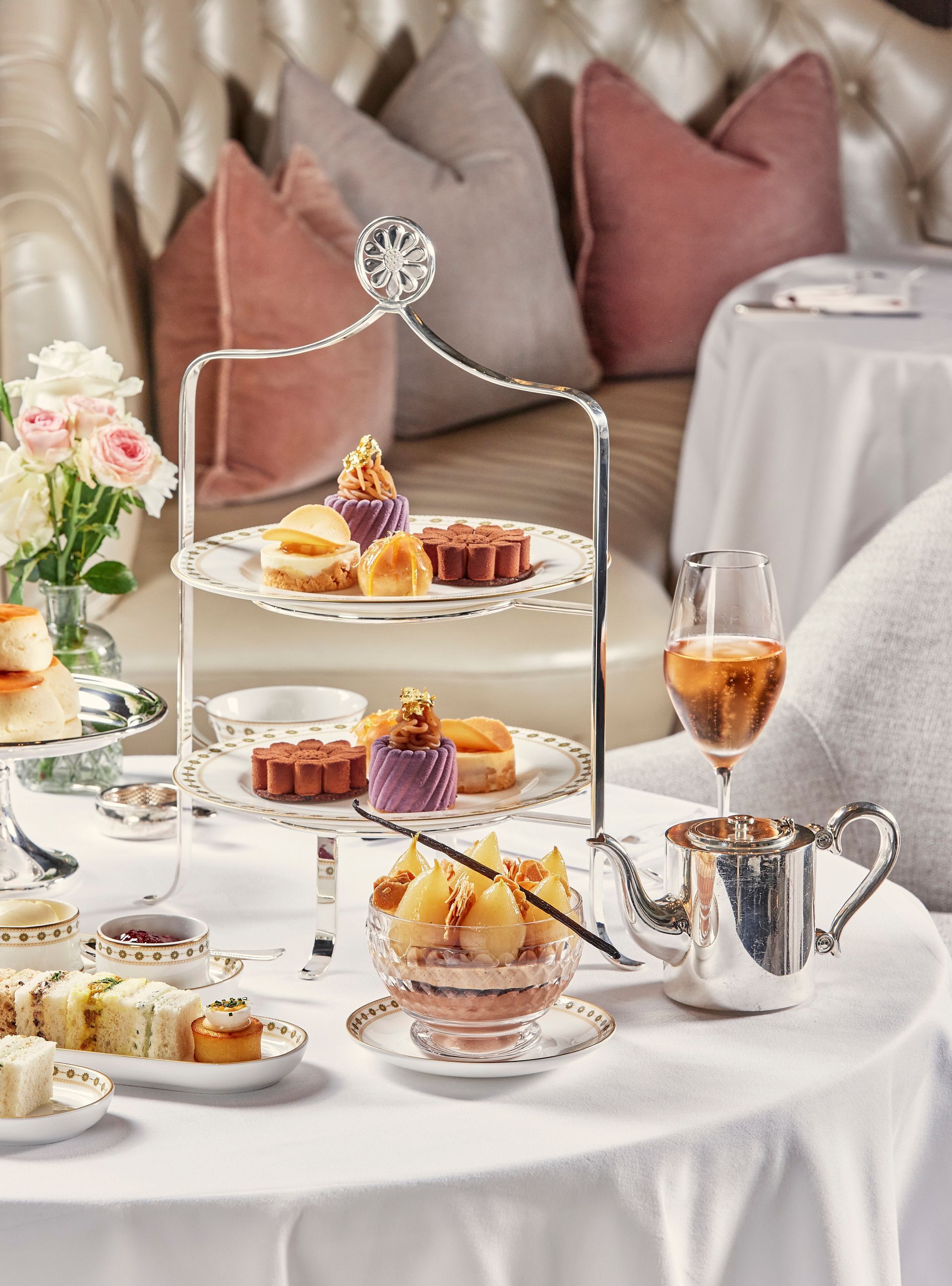 Elegant table set for tea with pastries, desserts, and champagne. Soft pink and beige decor.