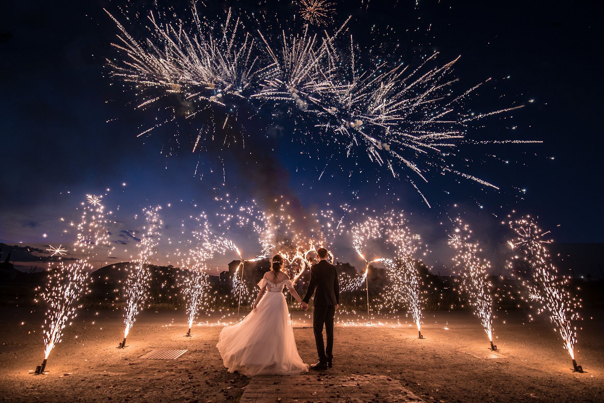 A bride and groom are standing in front of a fireworks display.