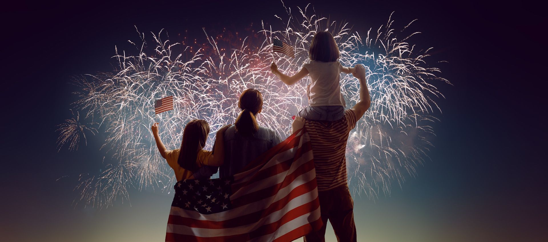 A family is watching fireworks on the fourth of july while holding an american flag.