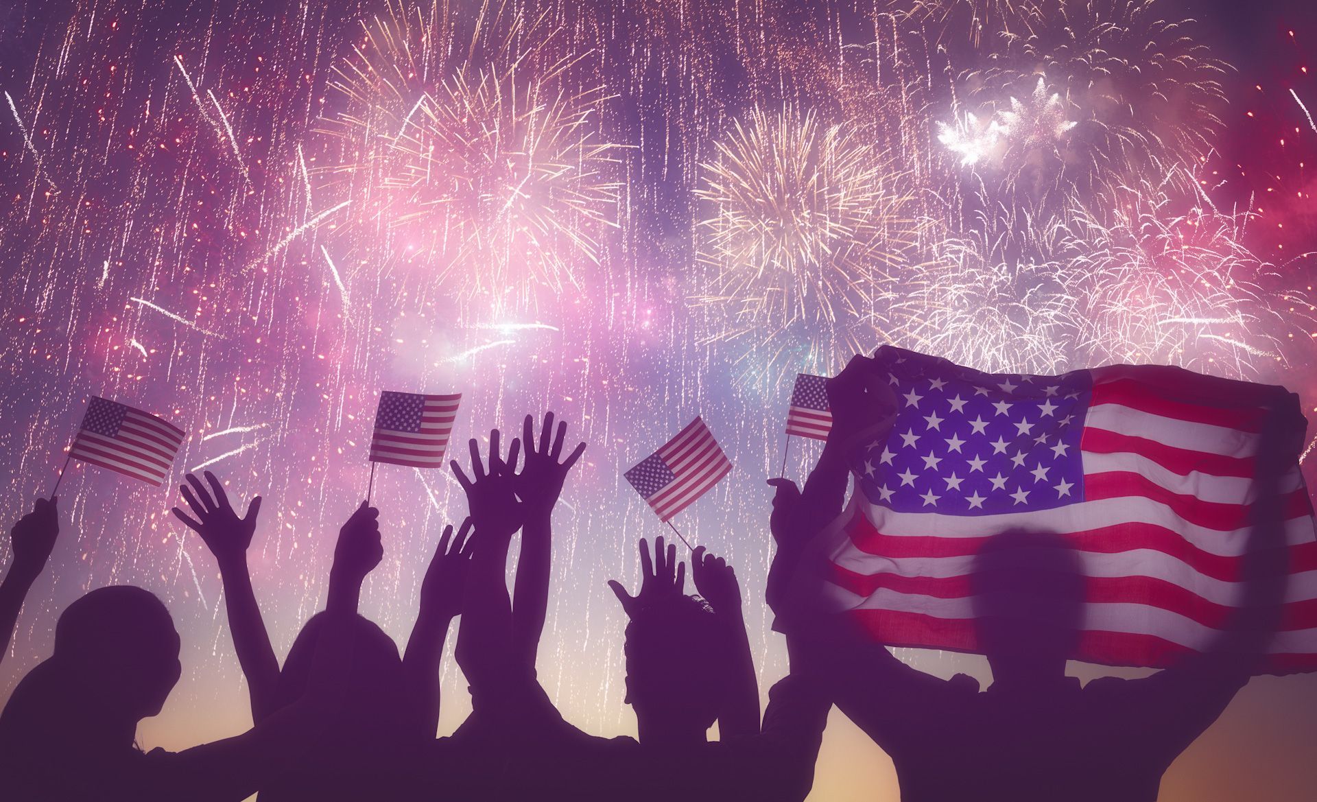 A group of people are holding American flags in front of a fireworks display.