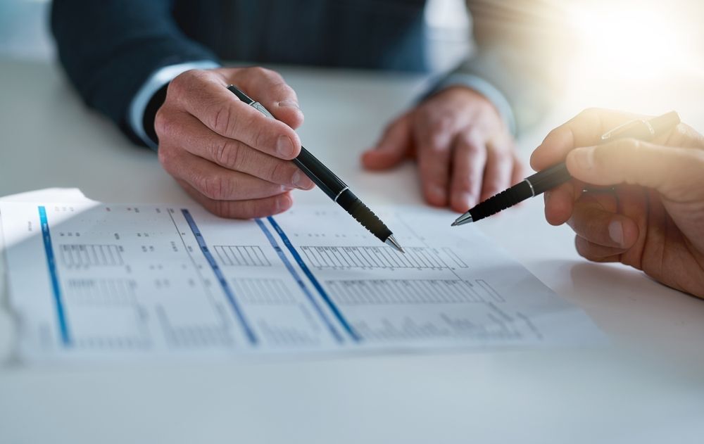 Hands pointing at a document on a table, discussing details.