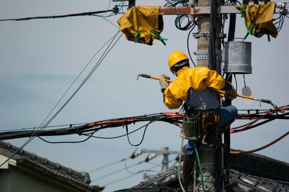 Lineman in Yellow Gear Working on Power Lines Atop a Utility Pole — Quaite Electrical Pty Ltd In Bundaberg, QLD