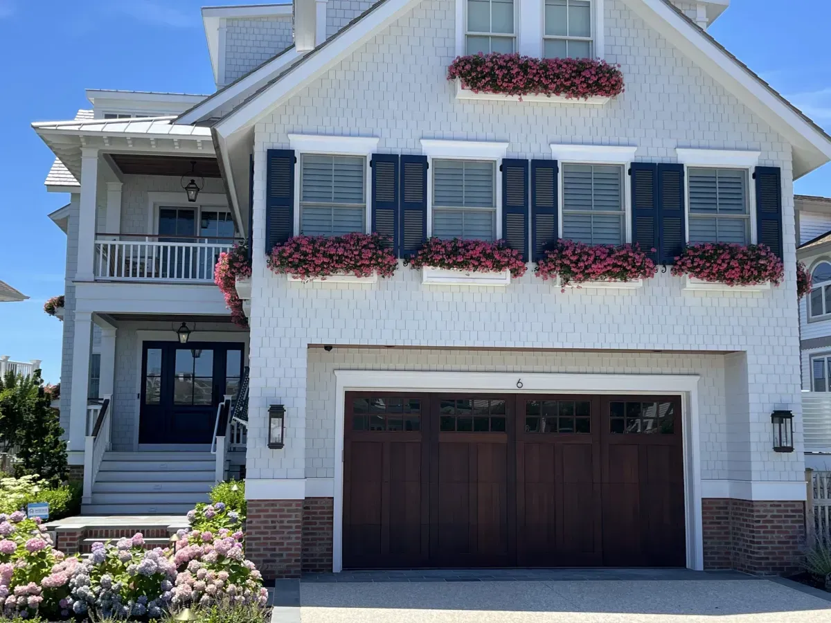 A white house with a brown garage door and black shutters.