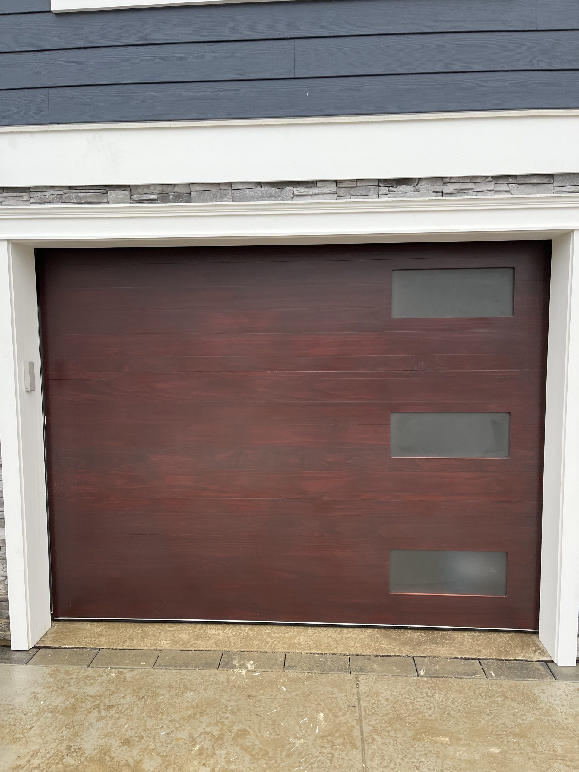 A wooden garage door with three windows is sitting in front of a house.