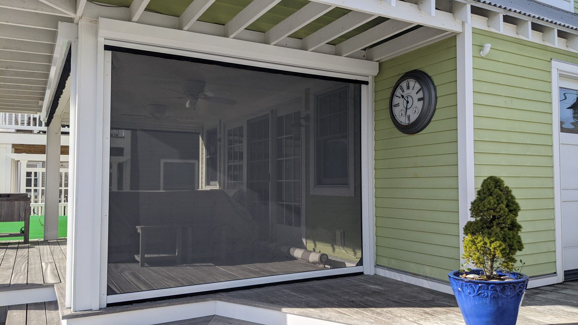 A screened in porch with a clock on the side of the house.