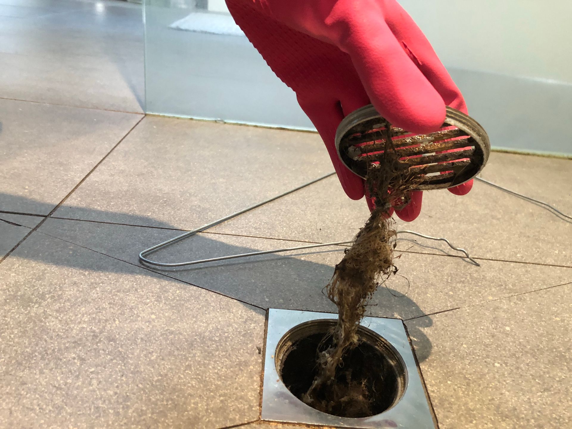 A person wearing red gloves is cleaning a drain with a brush.