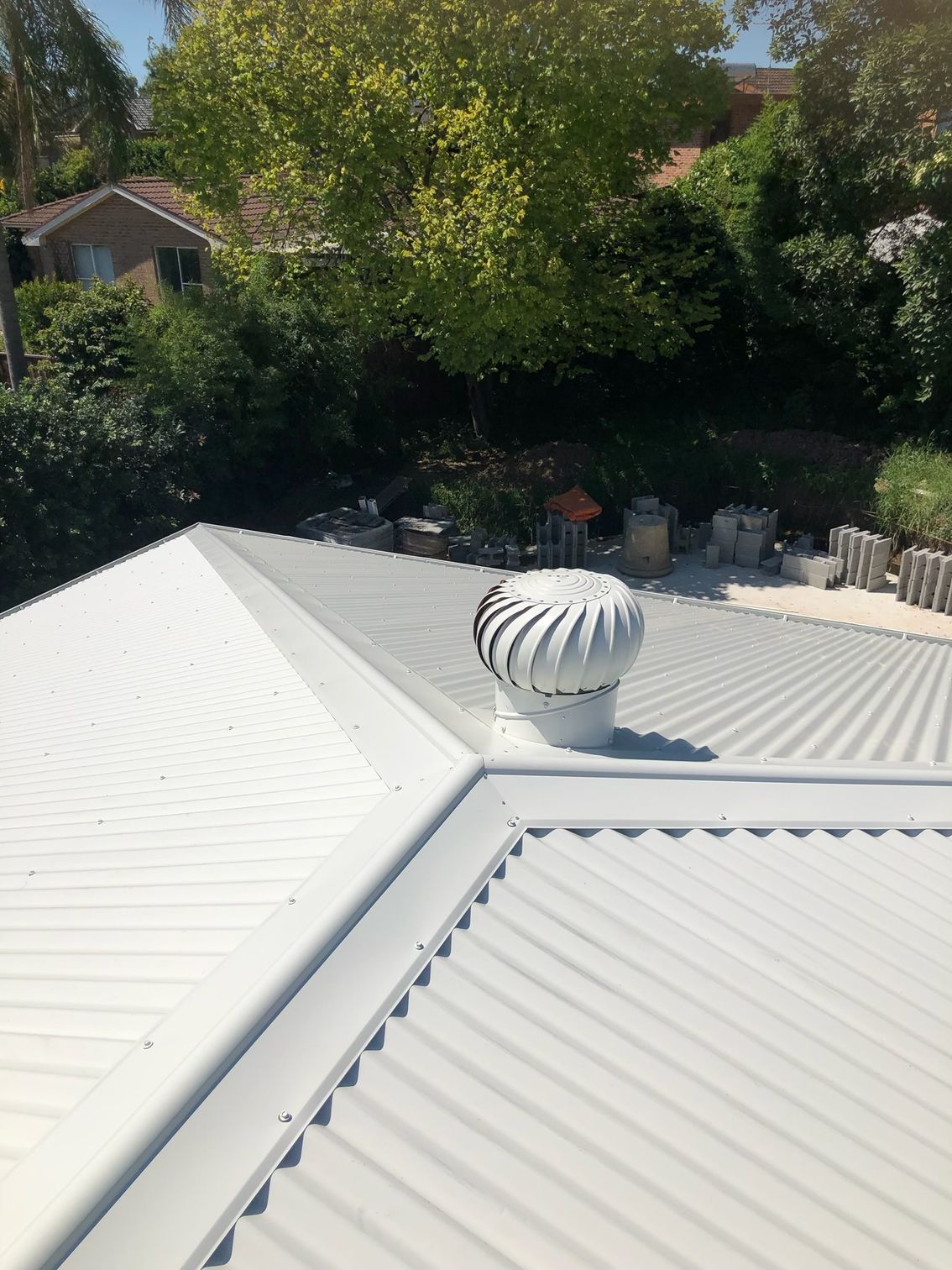 White metal roof with a spinning vent; trees and houses in the background.