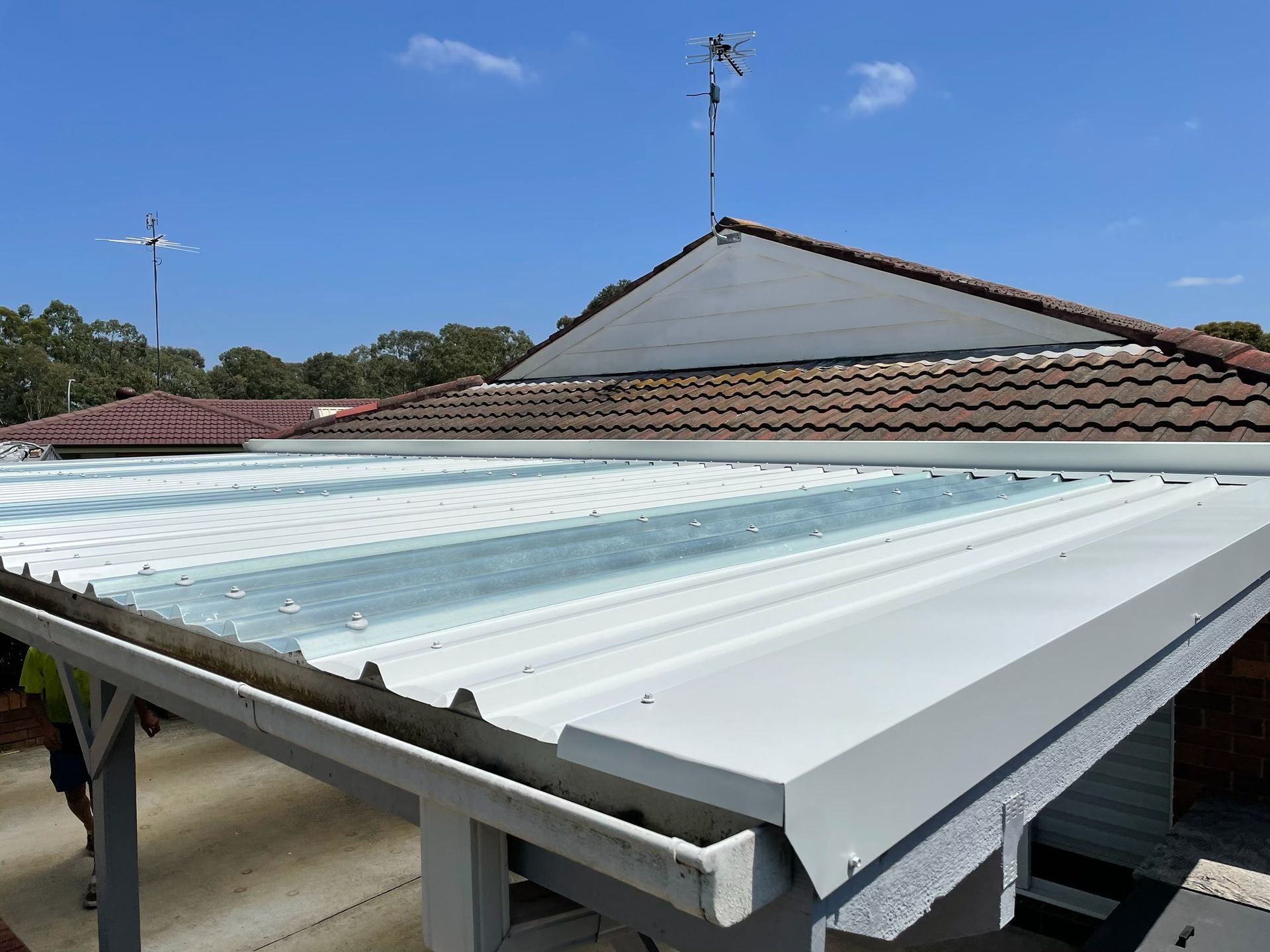 White metal carport roof attached to a home with a terracotta tiled roof. Blue sky in the background.