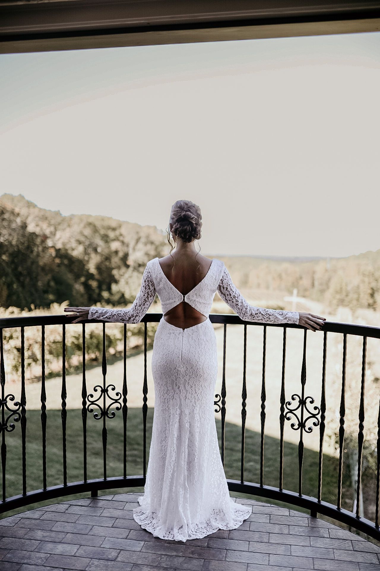 A woman in a wedding dress is standing on a balcony looking out over a lake.