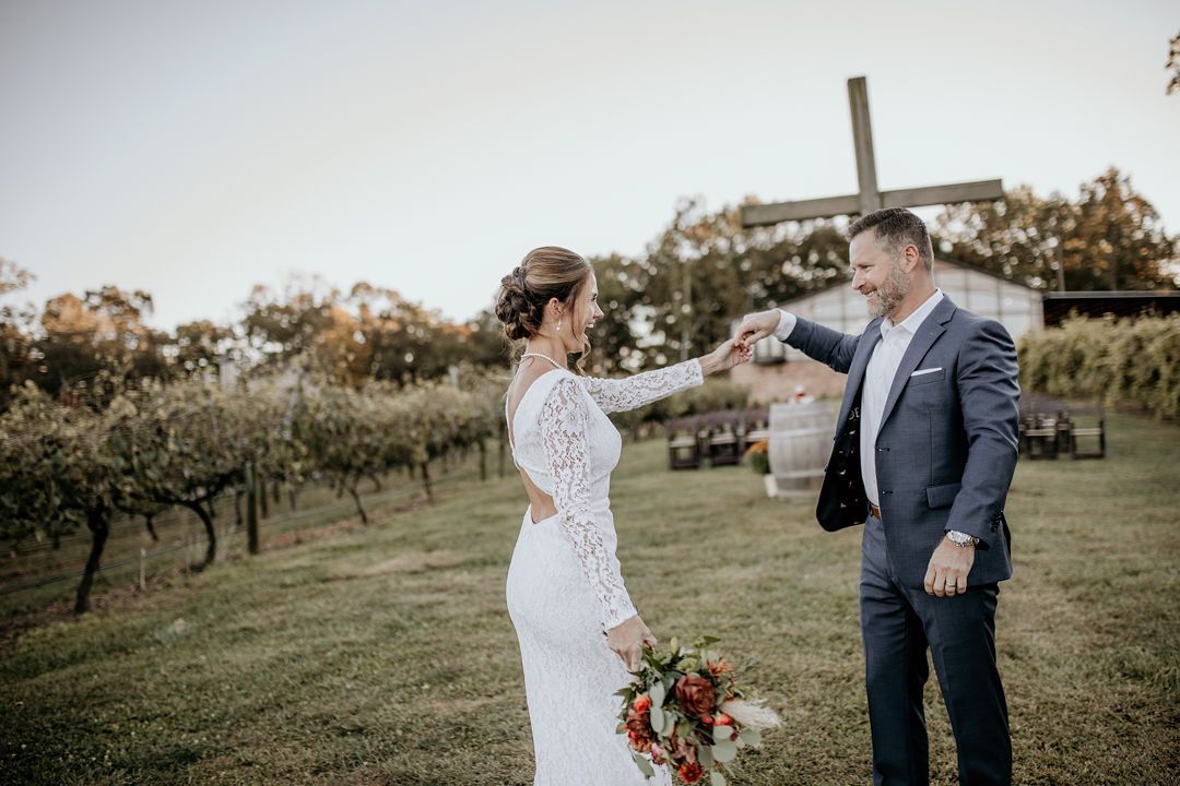A bride and groom are dancing in a field with a cross in the background.