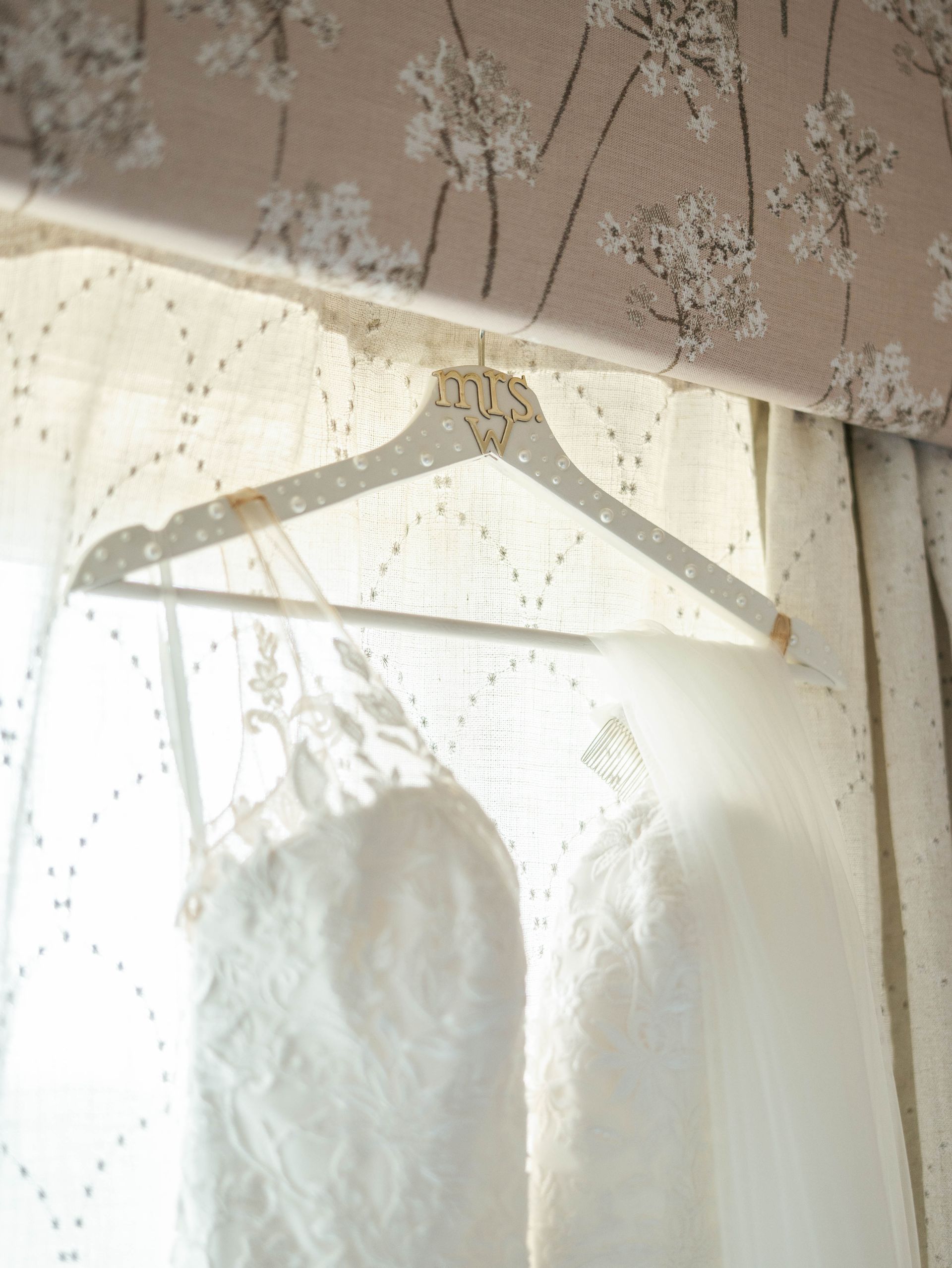 A white dress is hanging on a hanger in front of a window