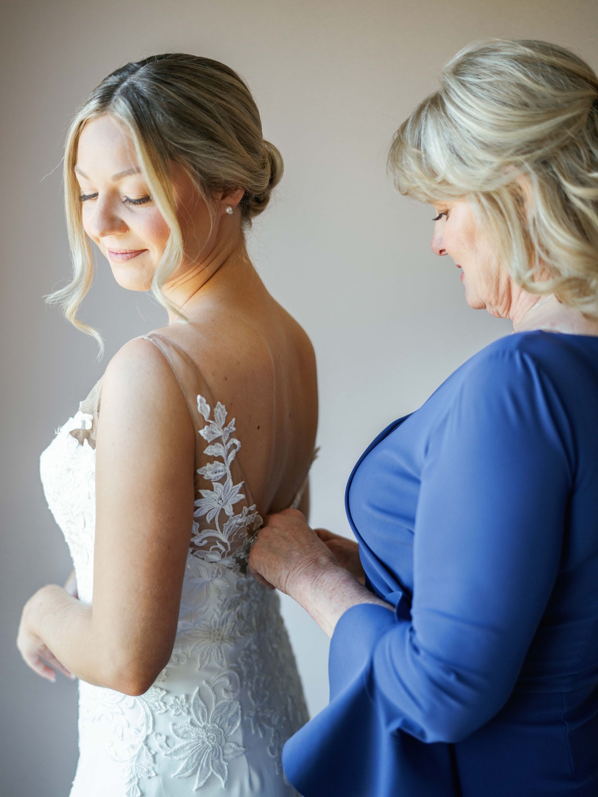 A woman in a blue dress helps a bride get ready for her wedding