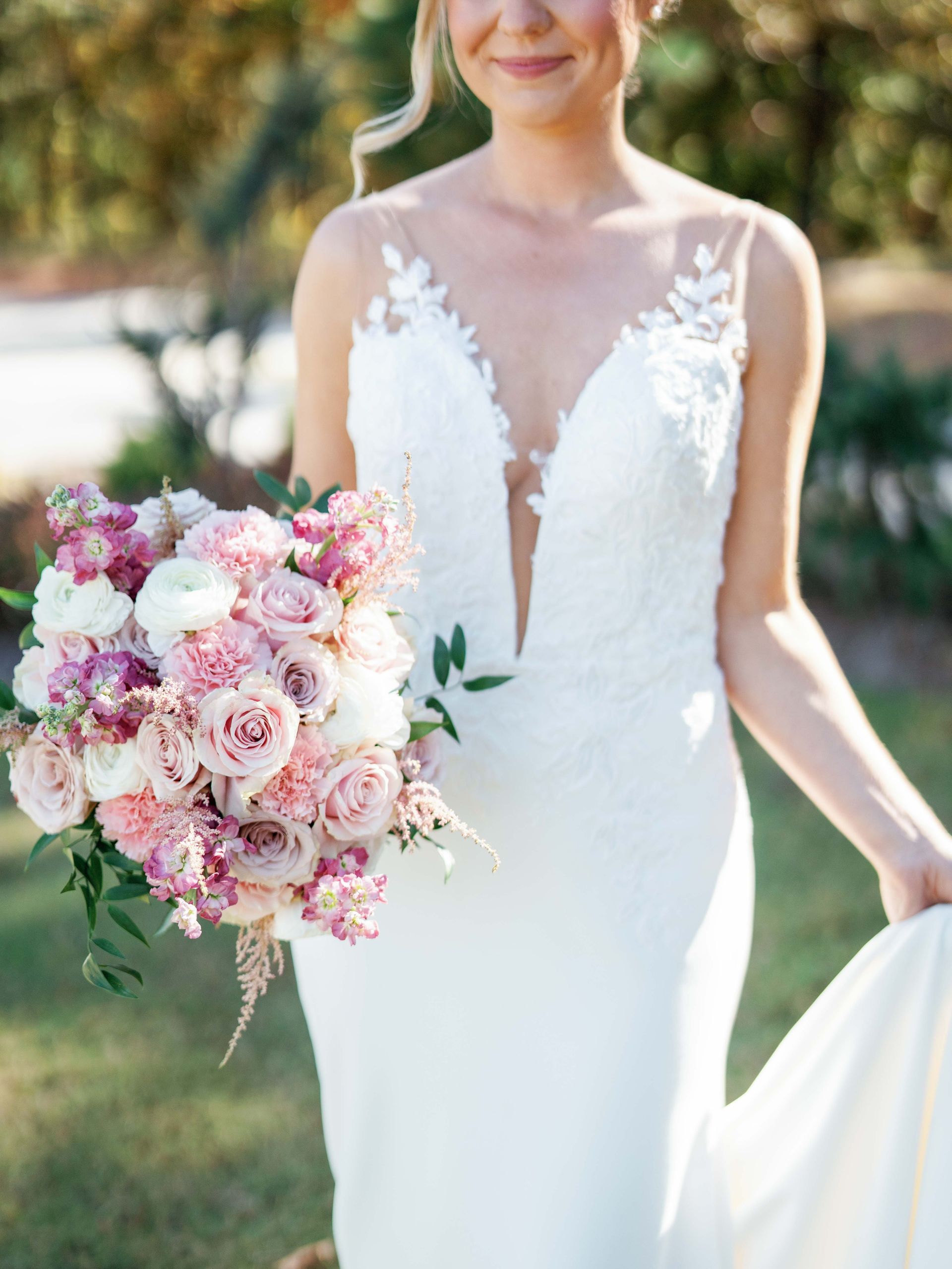 A bride in a white dress is holding a bouquet of pink and white flowers.