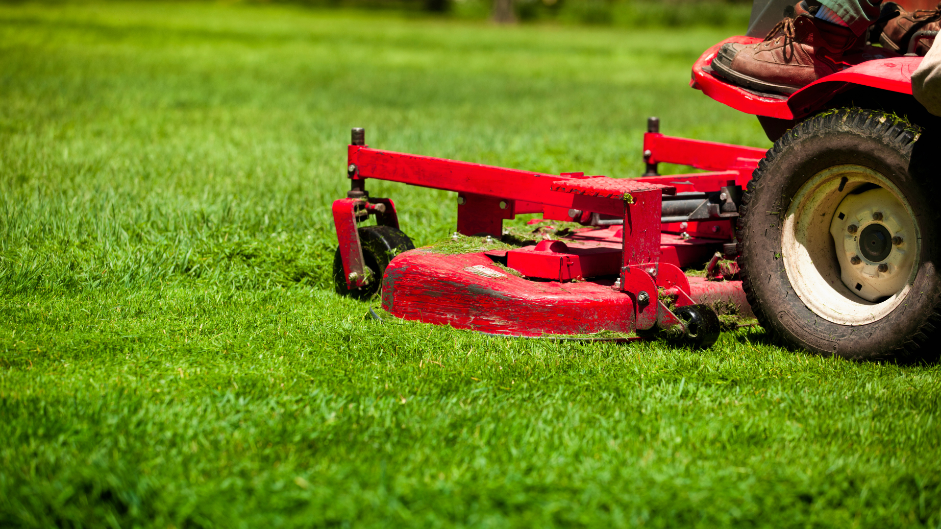 Red riding lawnmower mowing green grass on a sunny day.